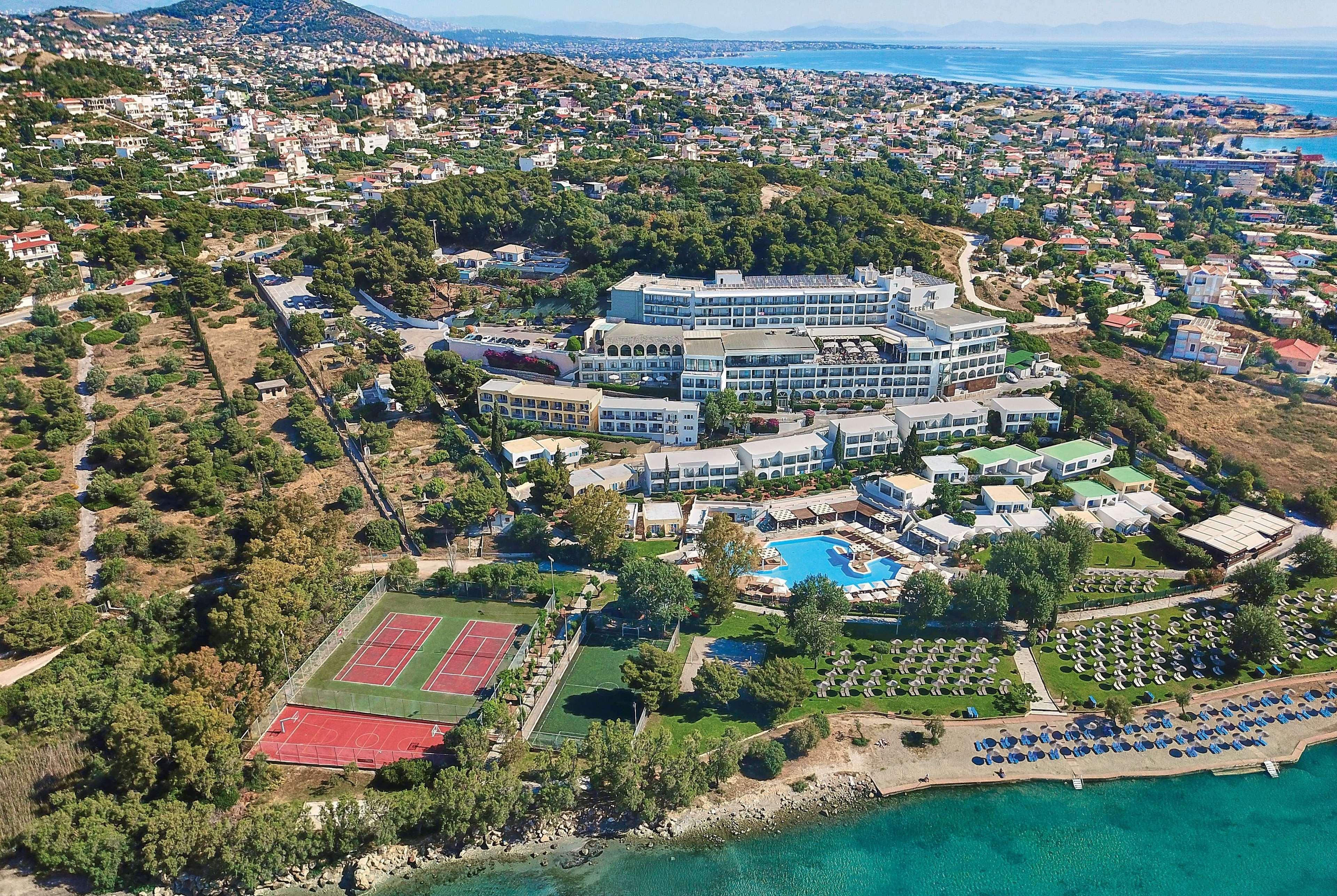 돌체 바이 윈덤 아티카 리비에라 호텔 브라브로나 외부 사진 The photo shows an aerial view of a resort or hotel complex situated near the coast. The building appears to be large, with multiple levels and several balconies. Surrounding the hotel are green landscaped areas, including gardens and perhaps a pool.